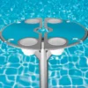 Vibrant BajaMate silicone placemats in blue, red, and beige displayed on a 24" aluminum entertainment table, designed to reduce heat and protect surfaces, arranged neatly on a baja shelf with a sparkling pool in the background.